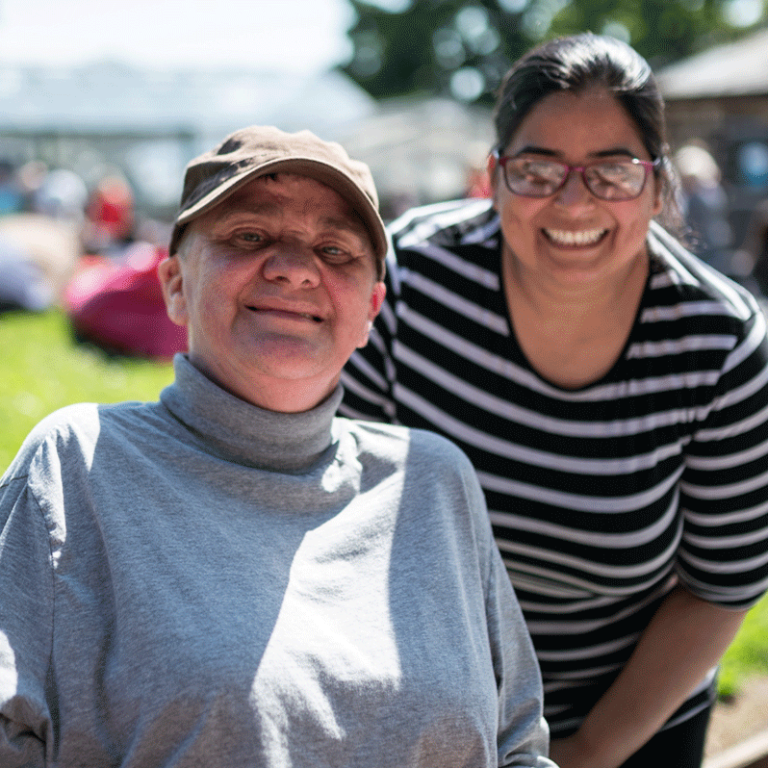 Smiling Asian lady posing outdoors in the sunshine next to an older person