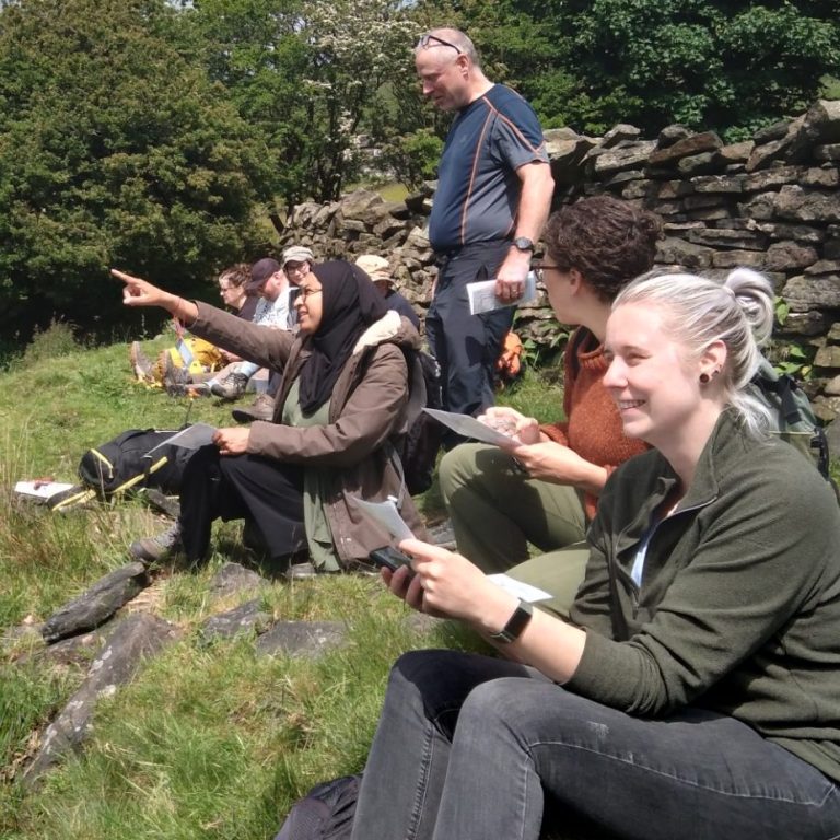 A diverse group of people sitting on the moors on a sunny day admiring the view